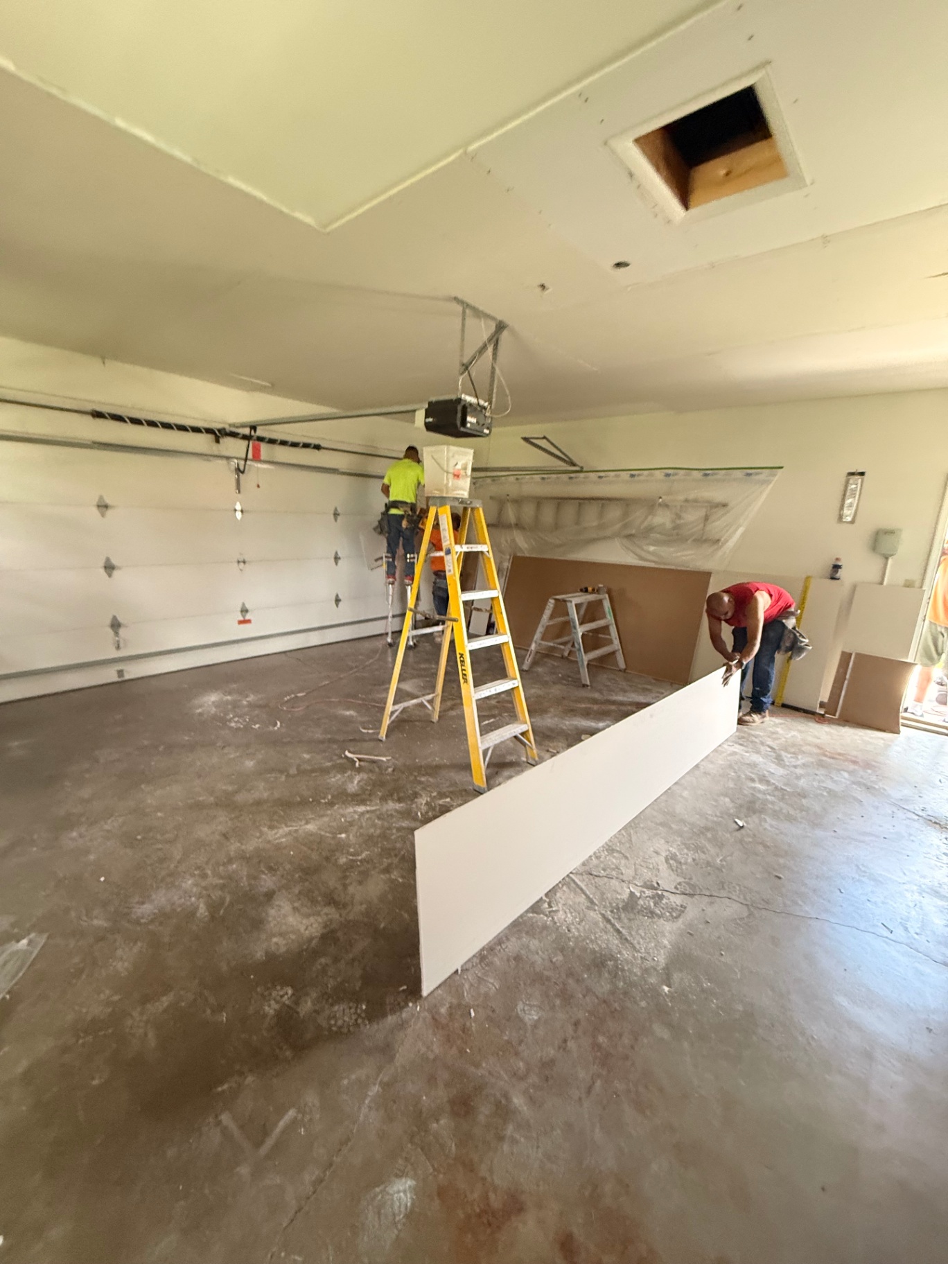 Crew laying out board on the floor as the first ceiling panels go up over the existing surface