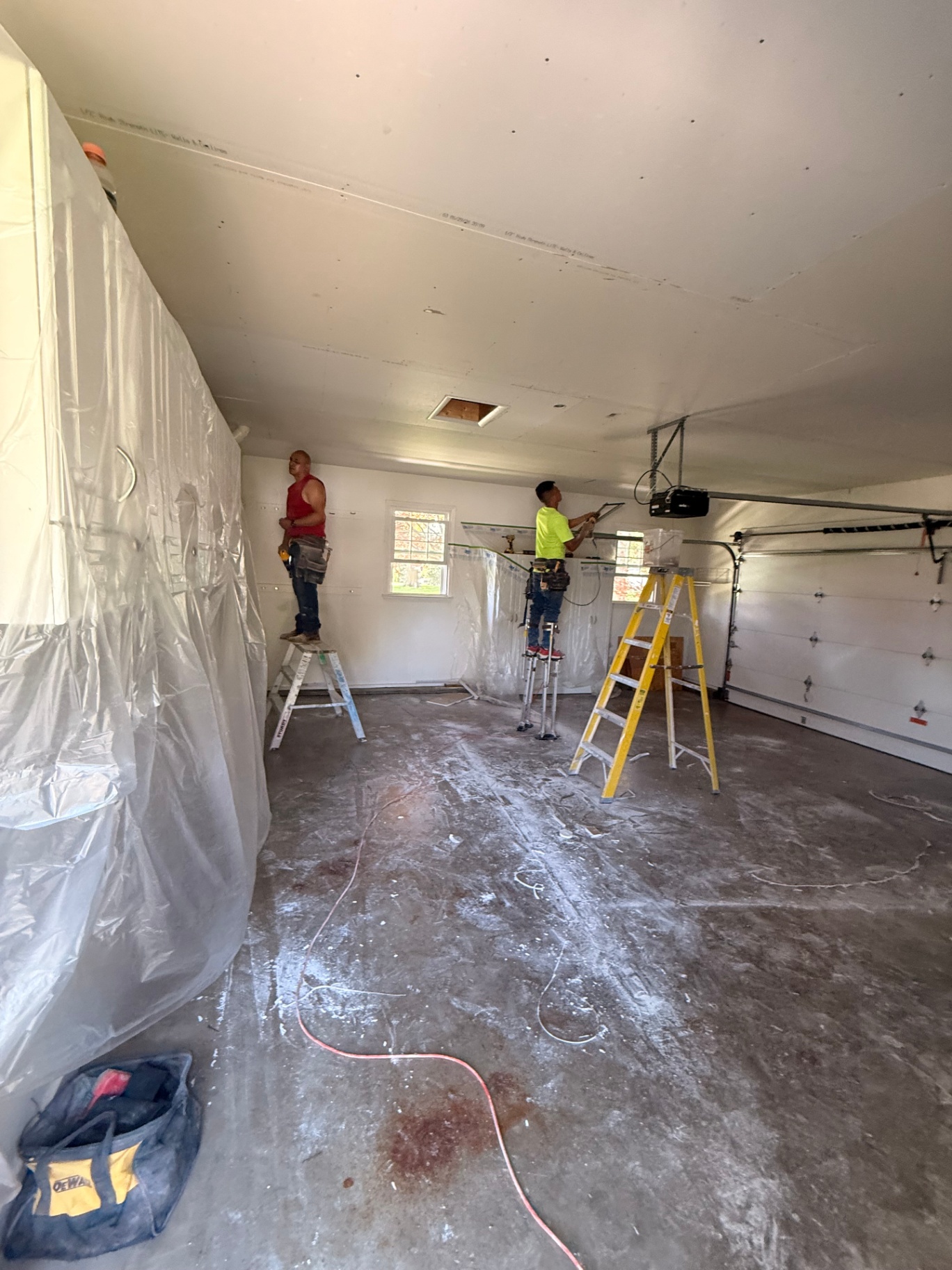 Hanging new drywall across the garage ceiling on stilts with walls fully masked off