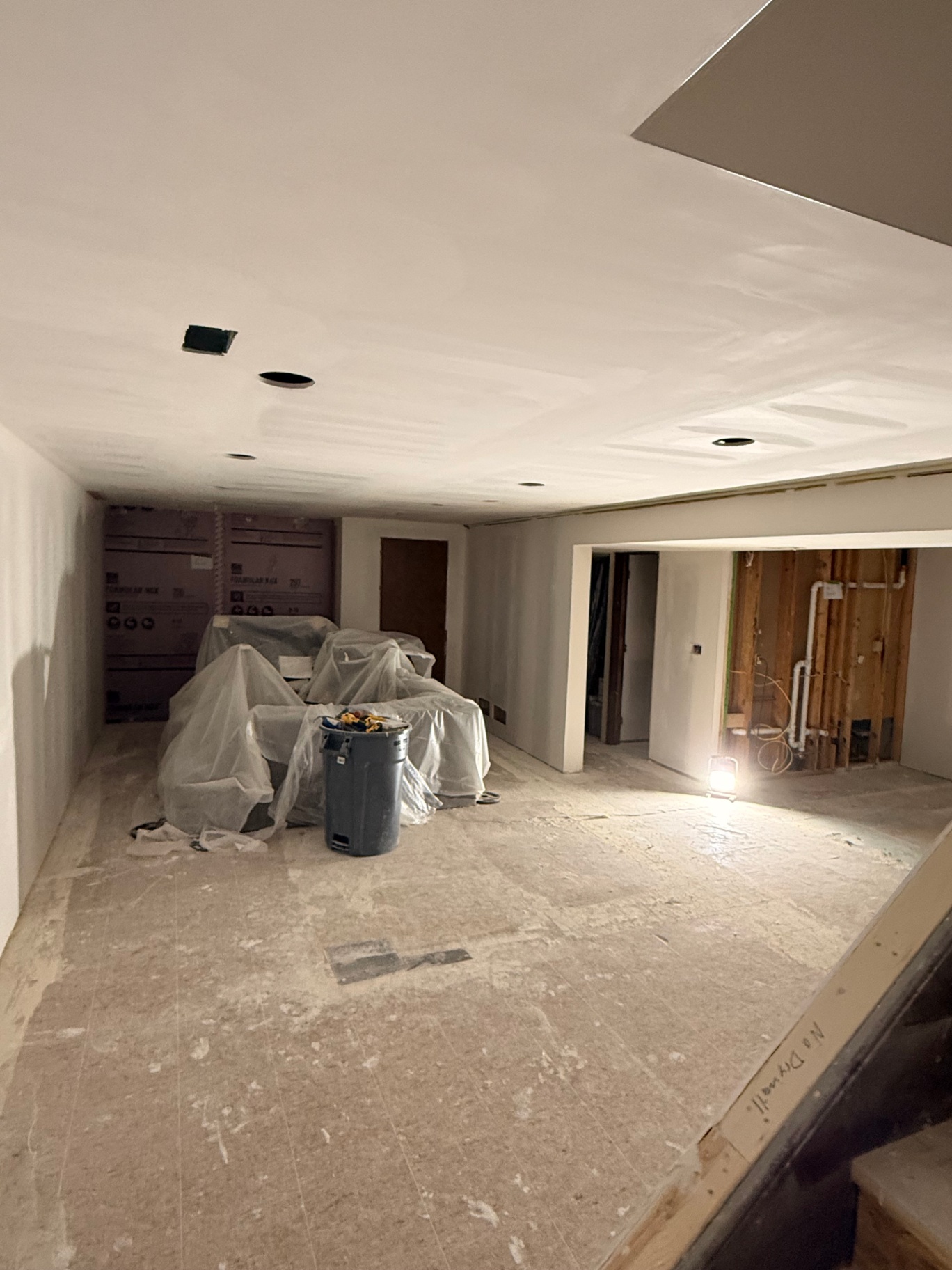 Wider view of the taped basement — ceiling and walls floated smooth with mud coats drying