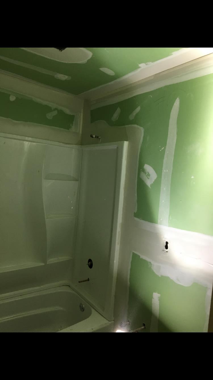 New tub surround set and walls boarded with moisture-resistant drywall — seams taped and ready for finish coats