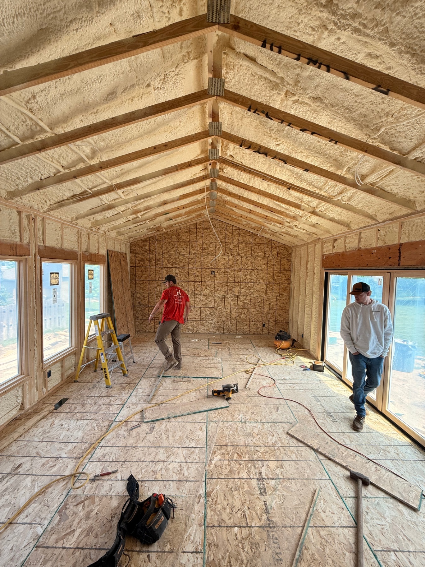 Bare framing with spray-foam insulation in place — crew laying out the vaulted addition before drywall