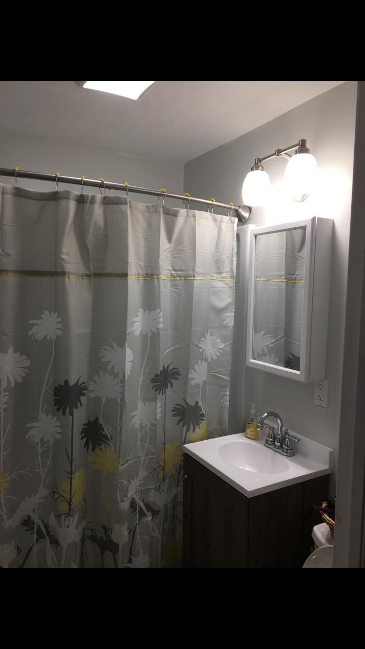 Finished bathroom from the vanity side — smooth painted walls, new medicine cabinet, lighting, and vanity in place