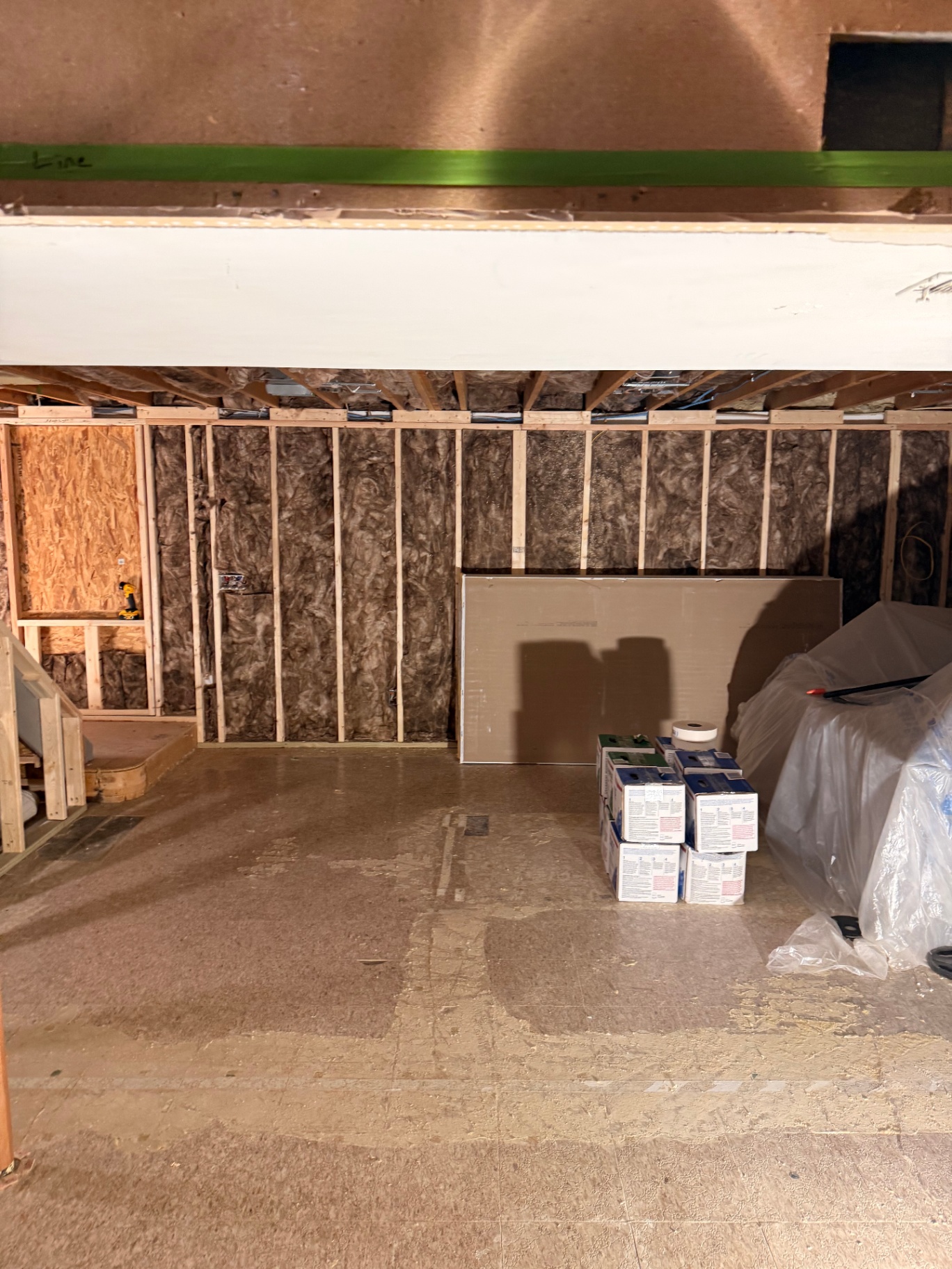 Framed basement staged with drywall, buckets, and mud boxes — furniture masked off ahead of the hang