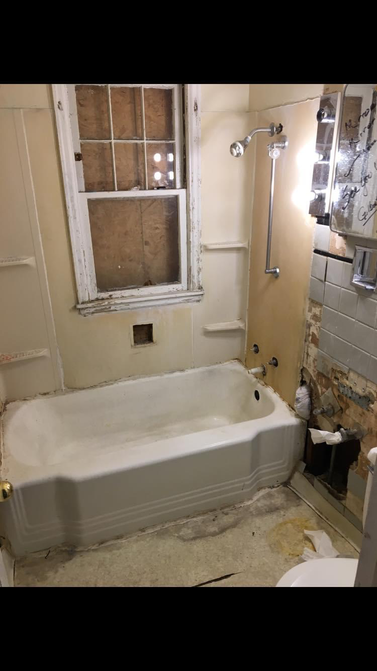 Original bathroom before demo — water-damaged walls around the tub and window with failing tile and trim