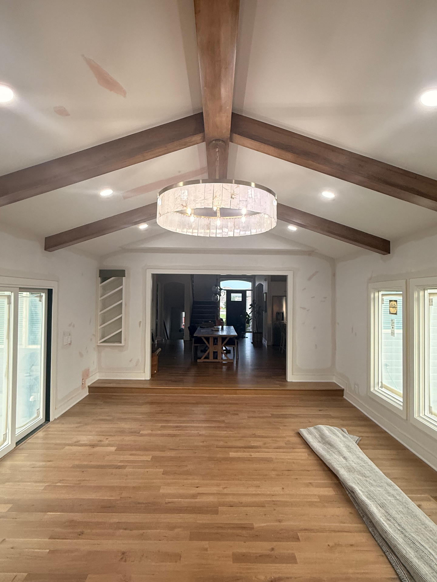 Completed addition — smooth painted walls and vaulted ceiling with stained beams and a chandelier, looking back toward the main house