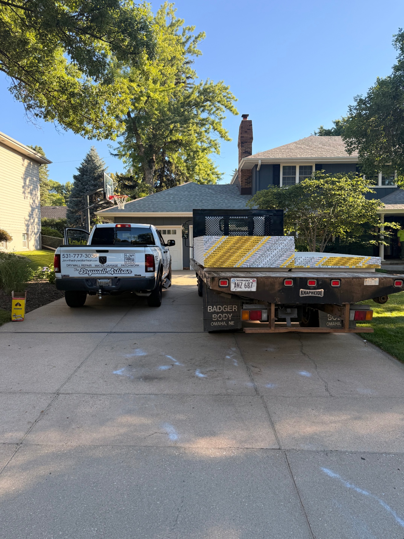 Drywall delivery on site — company truck and flatbed staged in the driveway before the basement hang