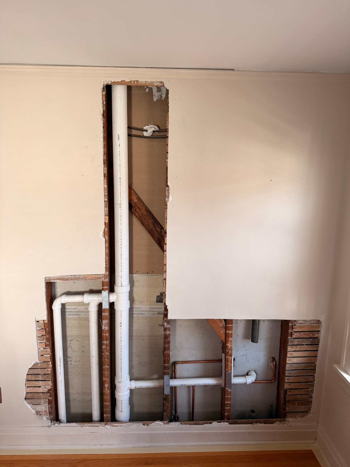 Wider view of the opened plaster wall with PVC and copper plumbing exposed for repair