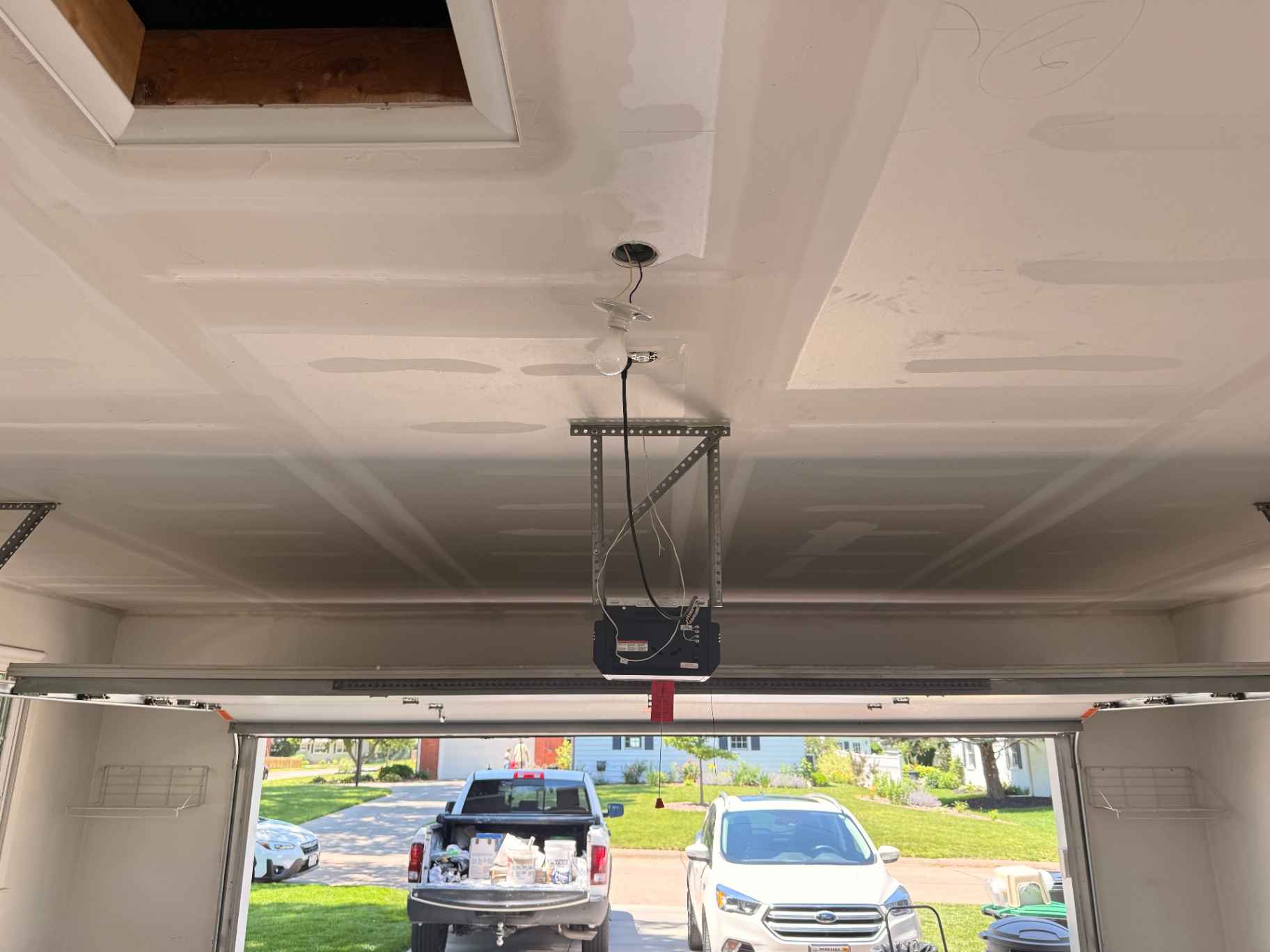 Finished garage ceiling — smooth, paint-ready drywall overlay with clean lines around the opener and attic opening