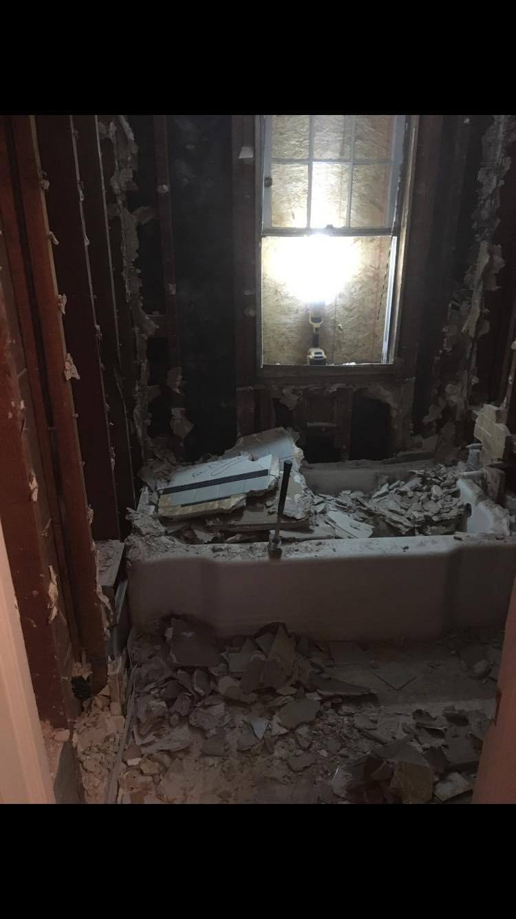 Bathroom gutted down to framing and subfloor — damaged plaster, lath, and substrate removed for rebuild