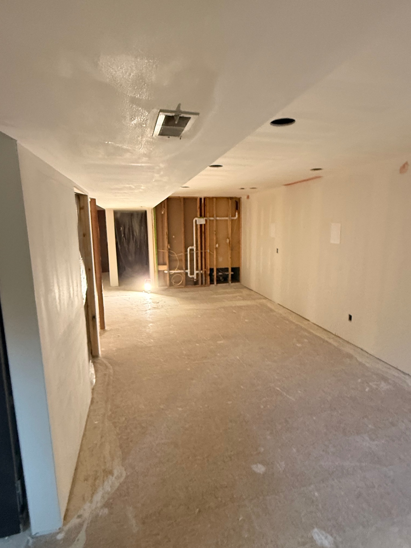 Basement hallway and ceiling primed white — recessed cans set and utility walls ready for paint
