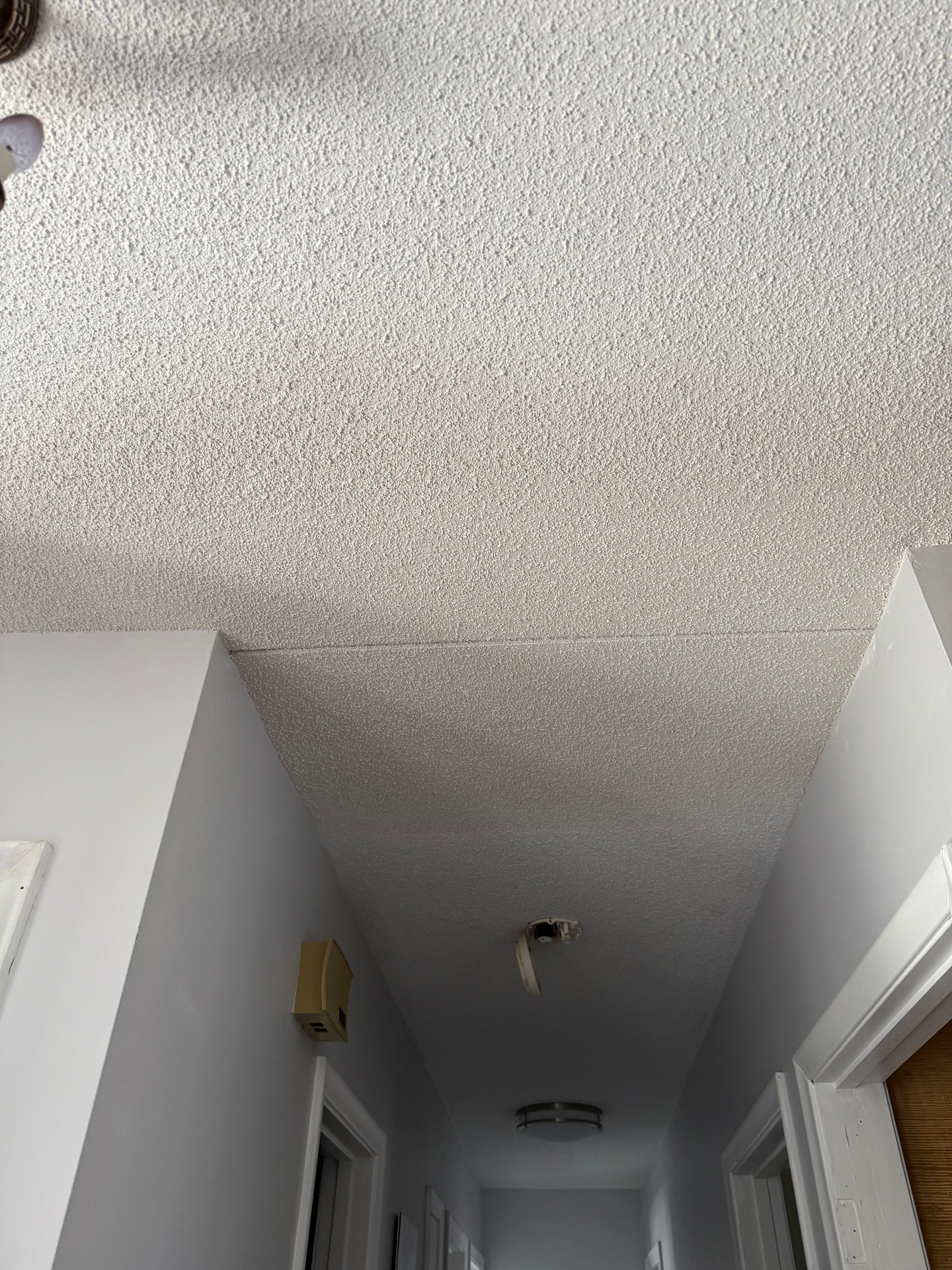 Drywall patch tied into the existing popcorn ceiling above a hallway opening — popcorn texture sprayed and blended to match the original